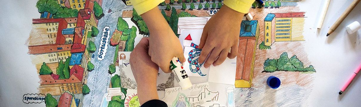 Vier Kinderhände basteln an einem bunten Plan für einen Spielplatz